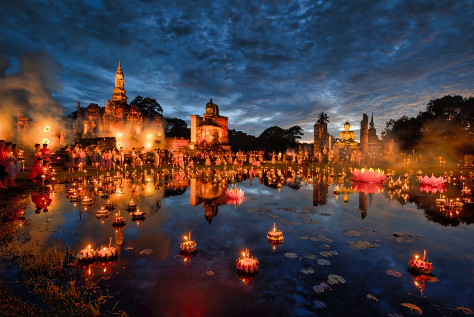 Candlelit krathong floating on the water at a temple during Loi Krathong